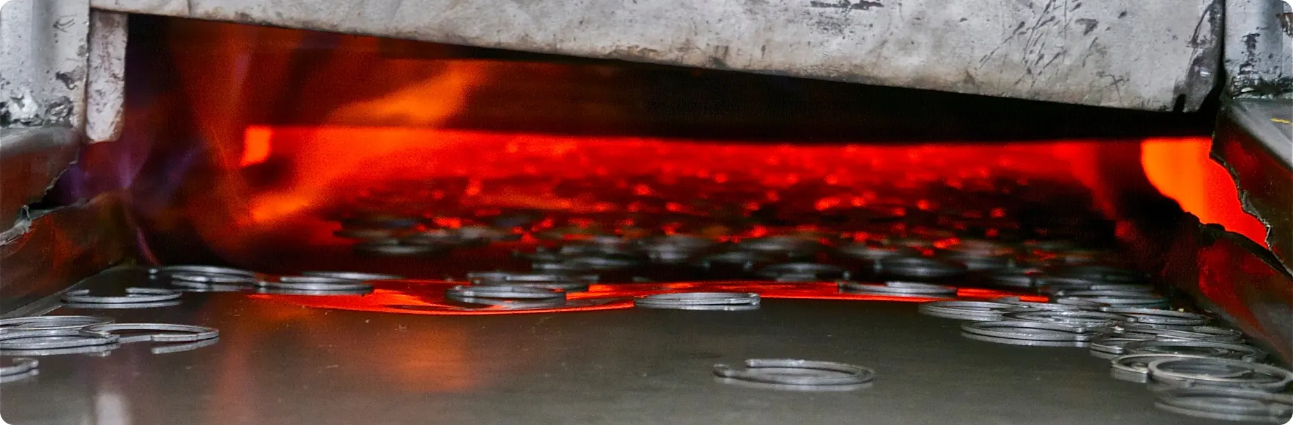 Piezas metálicas incandescentes saliendo del horno de temple